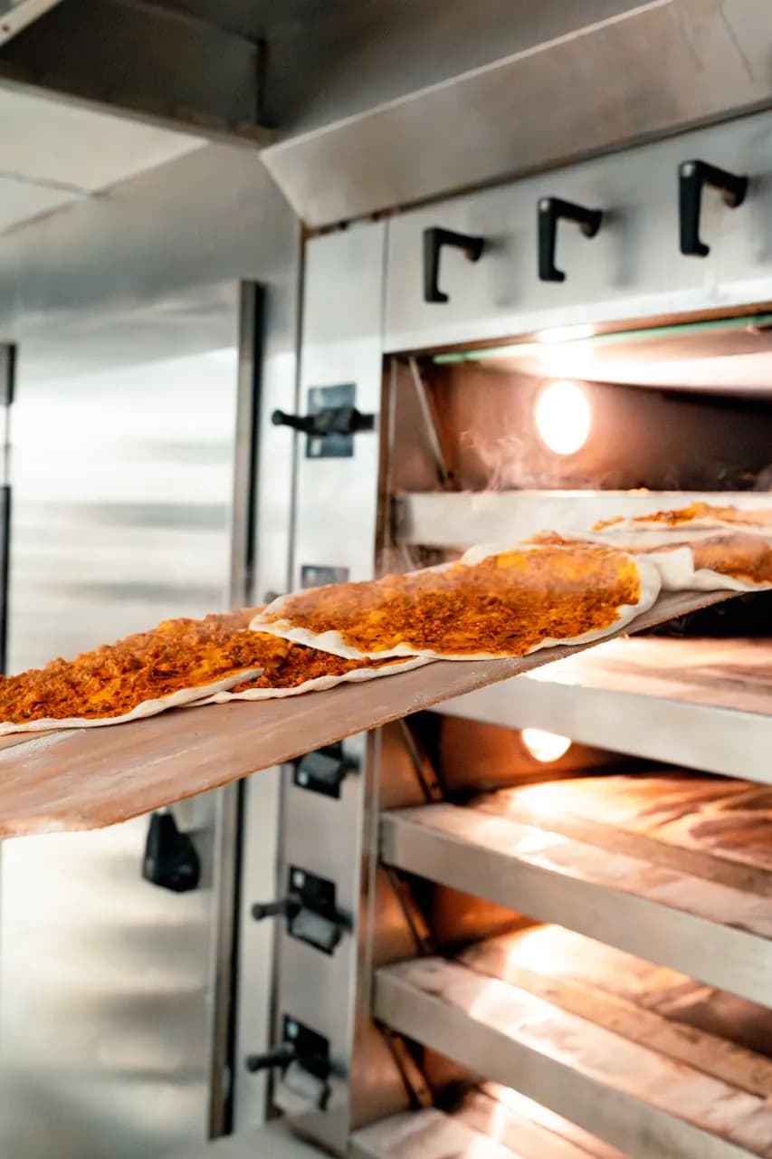 Lahmacun auf einem Holzschieber vor dem geöffneten Etagenofen